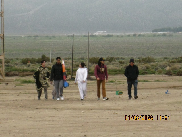 Five LBR members walking across the desert toward the launch pad carrying a rocket