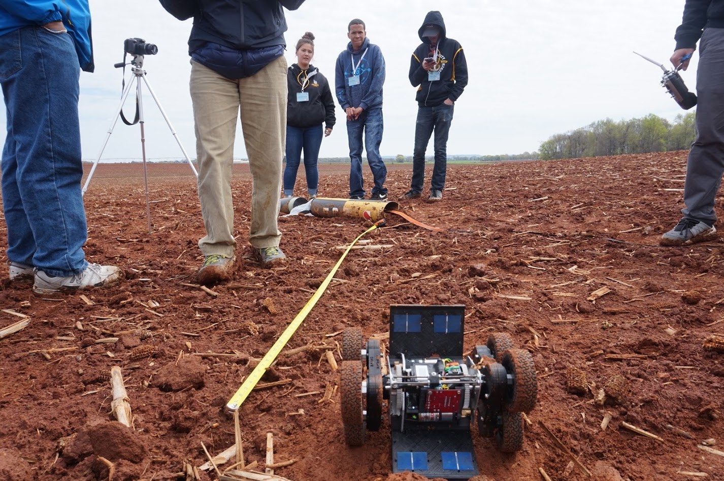 Payload recovery rover approaching a rocket in the field while team members look on